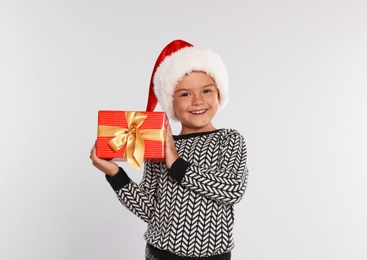 Happy little child in Santa hat with gift box on light grey background. Christmas celebration