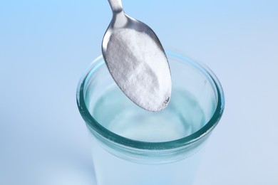 Photo of Adding baking soda into glass of water on light blue background, closeup