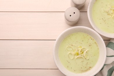 Photo of Bowls of tasty leek soup on white wooden table, flat lay. Space for text