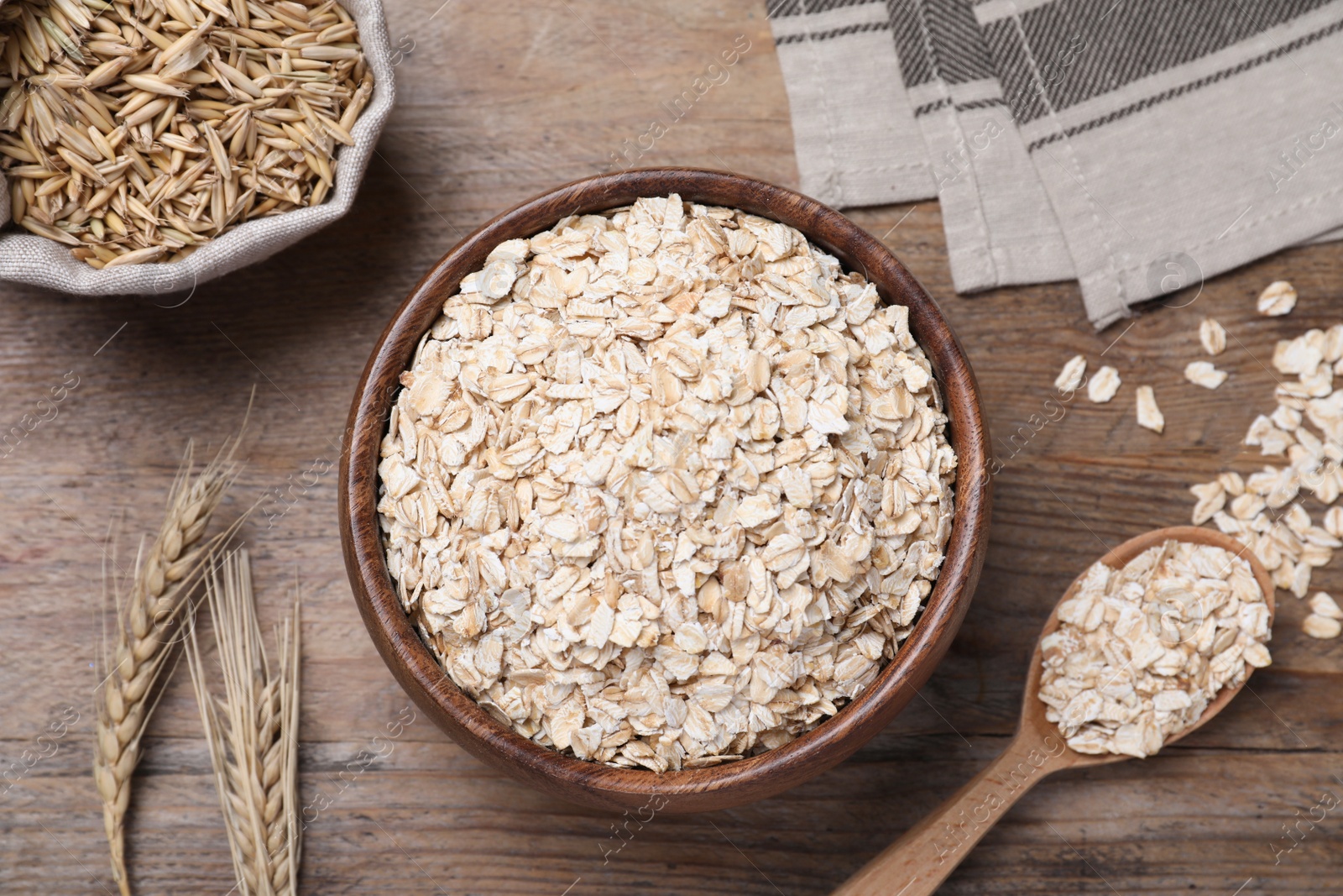 Photo of Oatmeal in bowl and spikelets on wooden table, flat lay