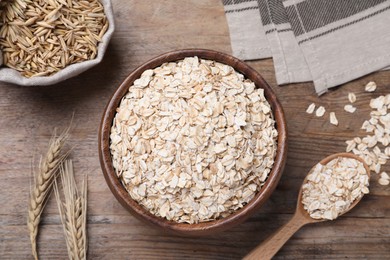 Photo of Oatmeal in bowl and spikelets on wooden table, flat lay