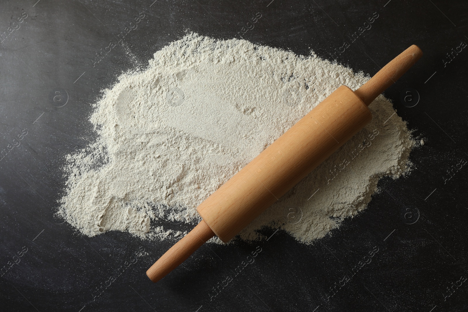 Photo of Flour and rolling pin on black table, top view