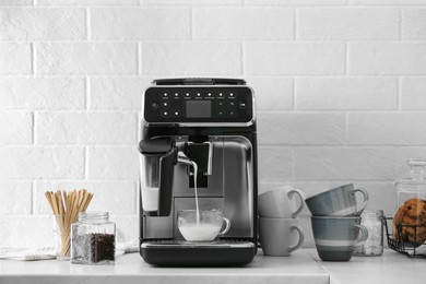 Photo of Modern coffee machine pouring milk into glass cup on white countertop in kitchen