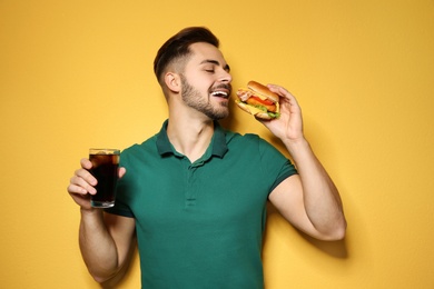 Handsome man with tasty burger and cola on color background
