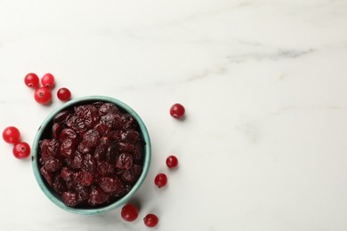 Photo of Tasty dried cranberries in bowl and fresh ones on white marble table, top view. Space for text