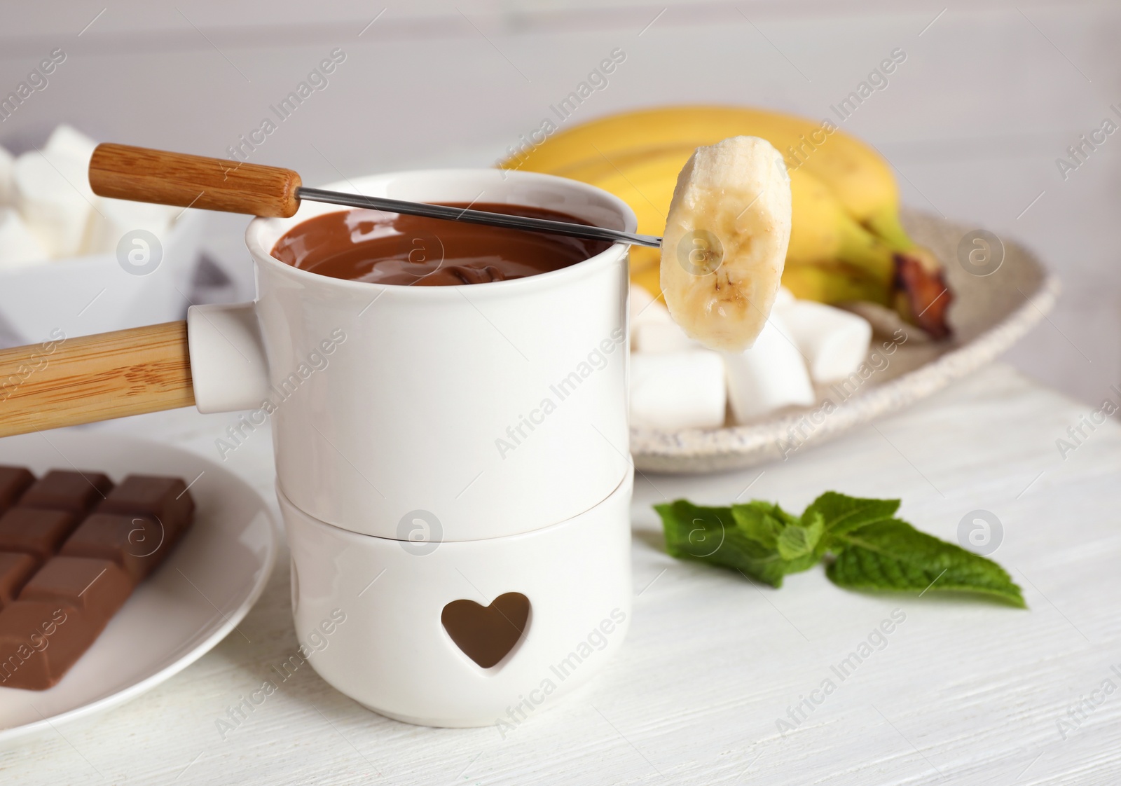 Photo of Fondue pot with chocolate and banana on white wooden table