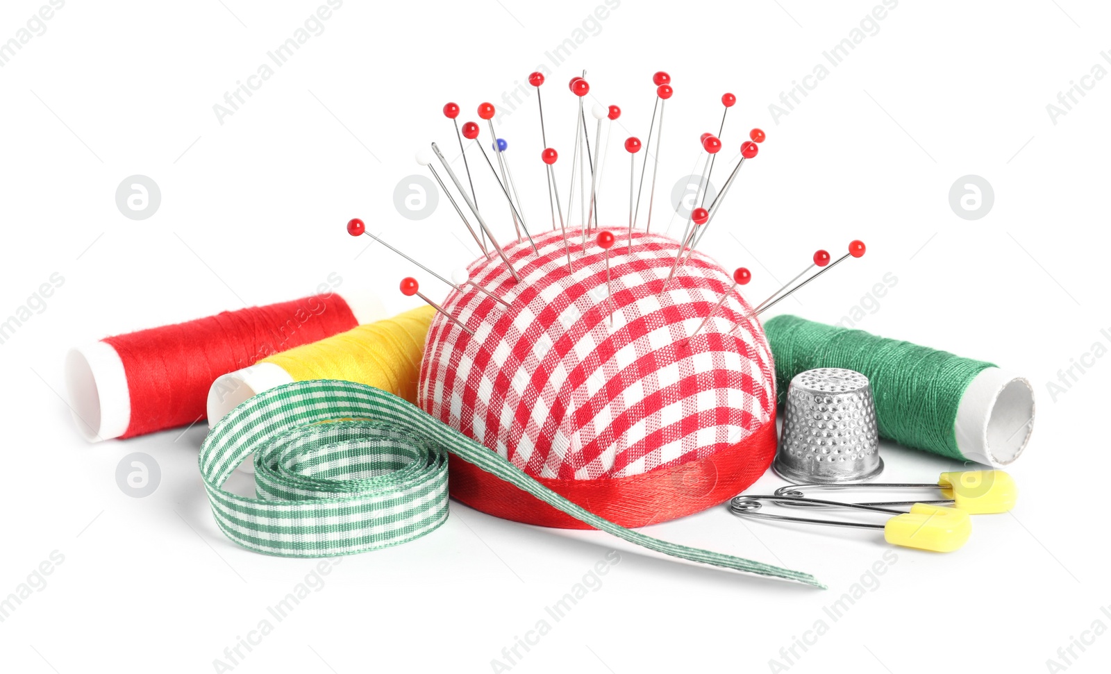 Photo of Checkered pincushion with sewing pins, spools of threads, ribbon and thimble isolated on white