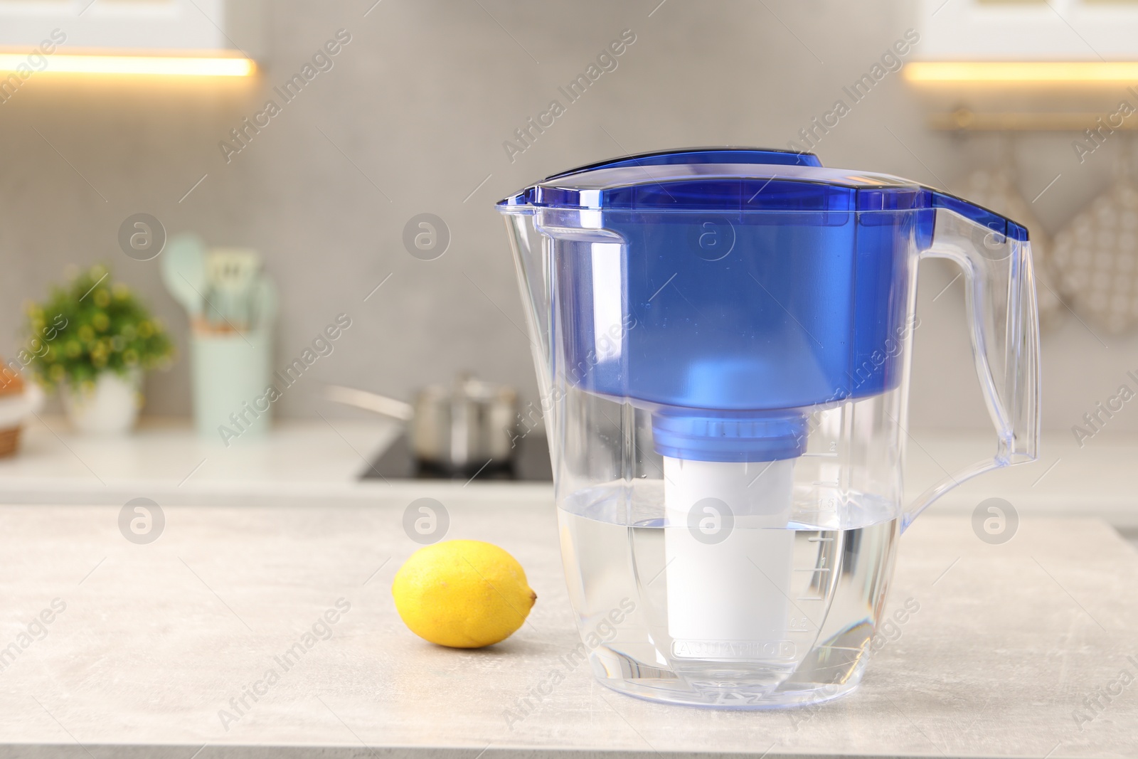 Photo of Water filter jug and lemon on light grey table in kitchen, space for text