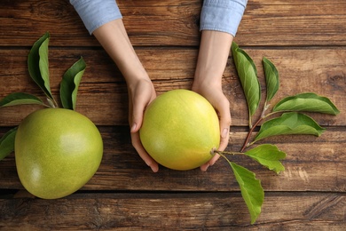 Photo of Woman holding fresh ripe pomelo at wooden table, top view