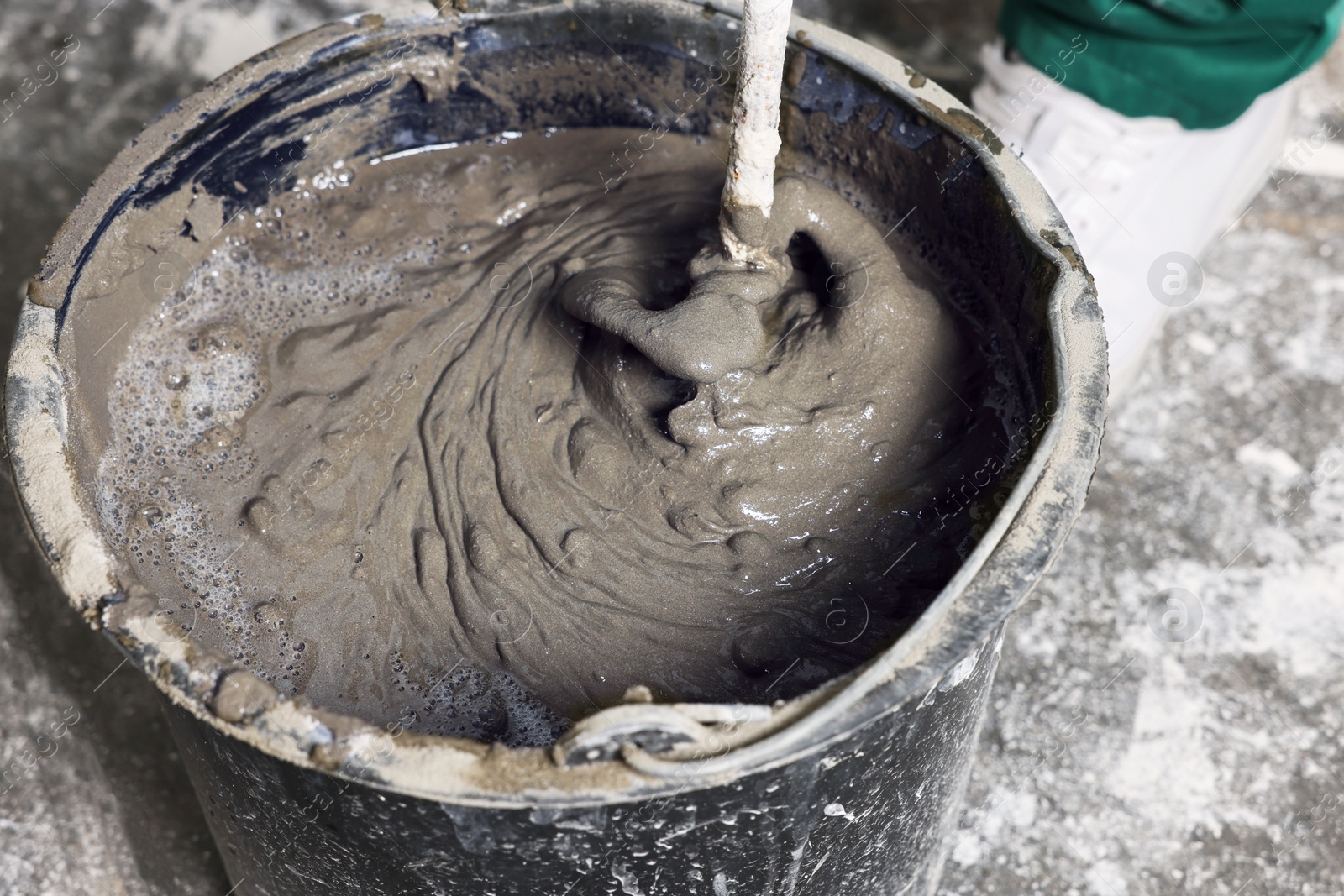 Photo of Worker mixing concrete in bucket indoors, closeup