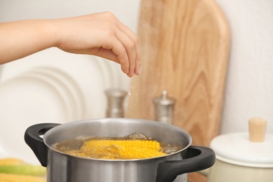 Photo of Woman salting water with corn cobs in stewpot, closeup