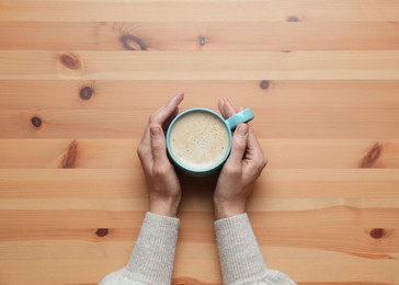 Photo of Woman with cup of coffee at wooden table, top view