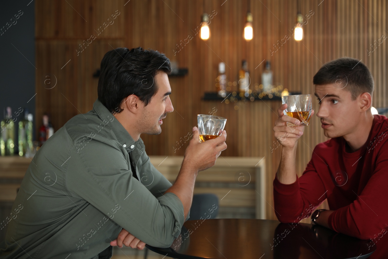 Photo of Young men drinking whiskey together in bar