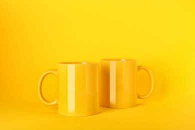 Photo of Two blank ceramic mugs on yellow background