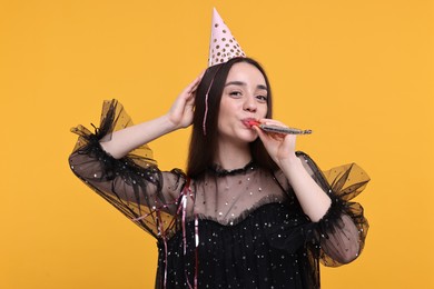 Woman in party hat with blower and streamers on orange background