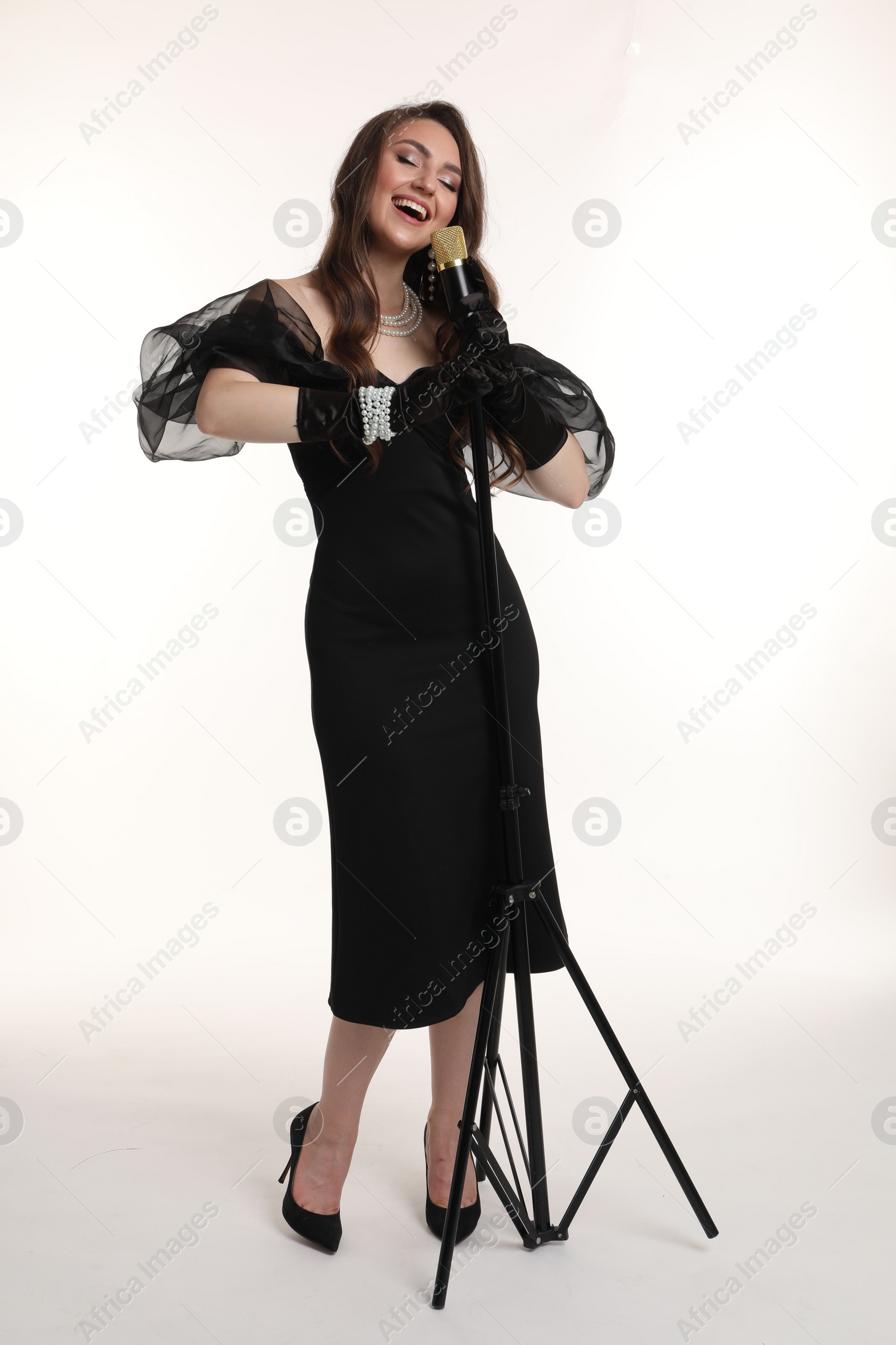 Photo of Beautiful young woman in stylish dress with microphone singing on white background