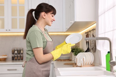 Photo of Happy young housewife with clean plate in kitchen. Cleaning chores