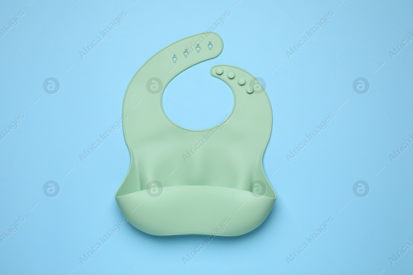 Photo of Green silicone baby bib on light blue background, top view. First food