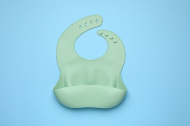 Photo of Green silicone baby bib on light blue background, top view. First food