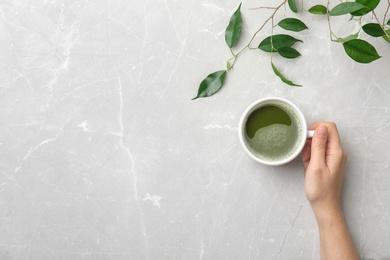 Photo of Woman with cup of matcha tea and leaves at table, top view