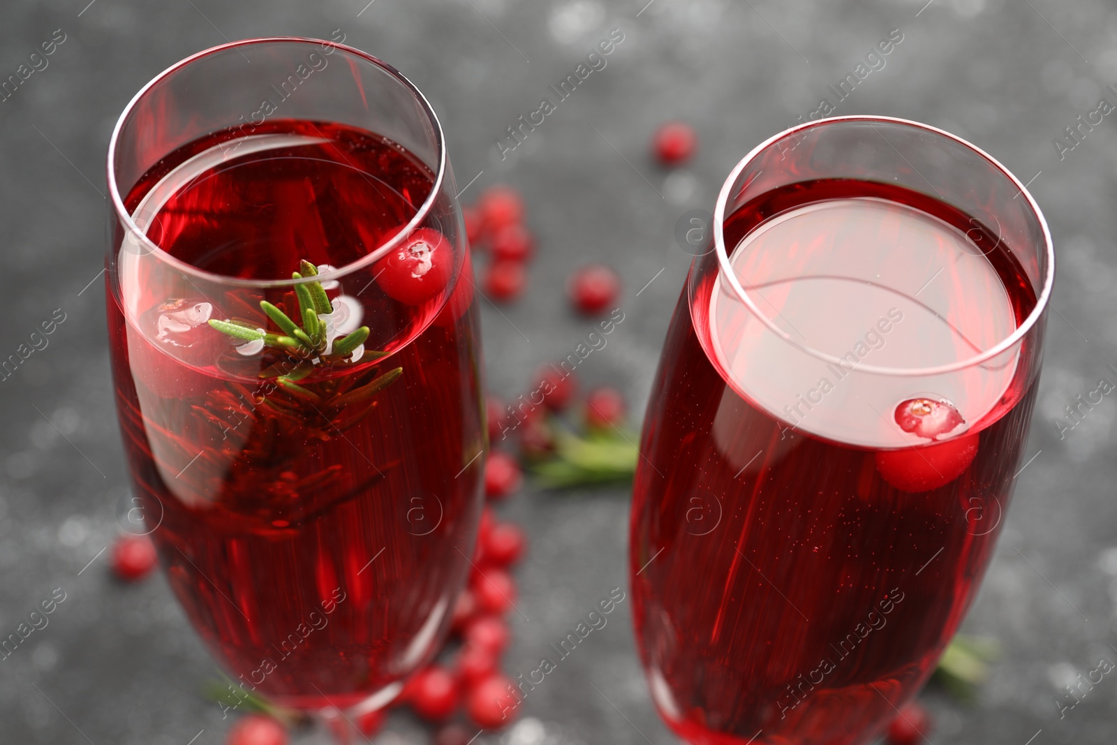 Photo of Tasty cranberry cocktail with rosemary in glasses on gray background, closeup