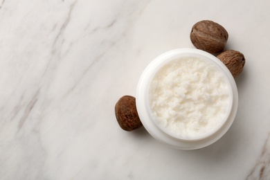 Jar of shea butter, nuts and space for text on marble background, top view