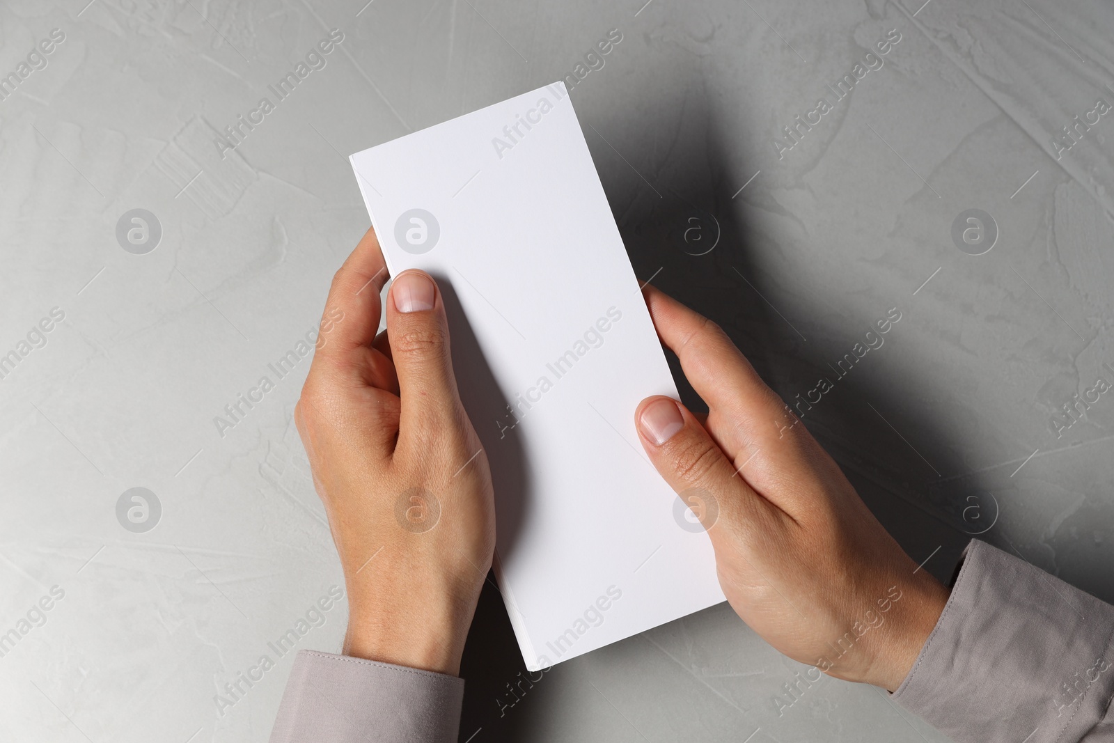 Photo of Man holding white blank card at light grey table, top view. Mockup for design