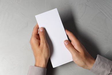 Photo of Man holding white blank card at light grey table, top view. Mockup for design