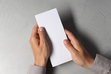 Man holding white blank card at light grey table, top view. Mockup for design