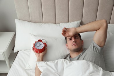 Photo of Man with alarm clock in bed. Being late because of oversleeping