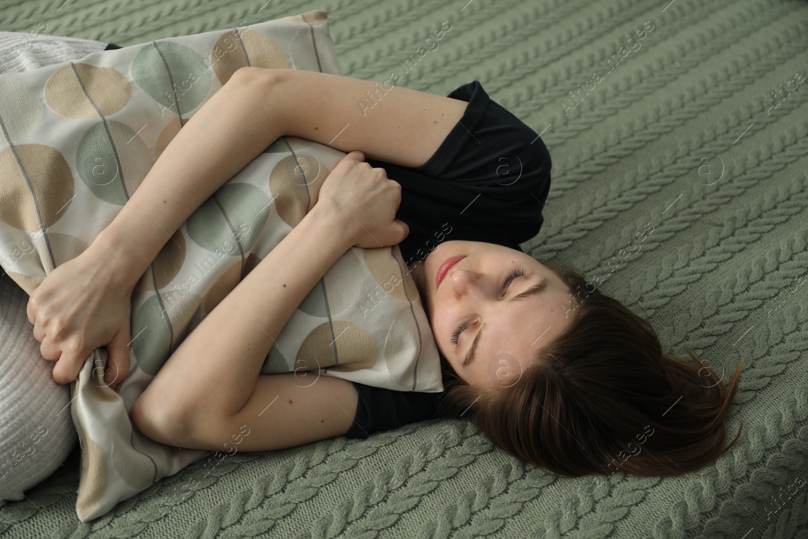 Photo of Sad young woman lying on bed at home