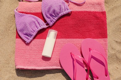 Photo of Beach towel with slippers, sunscreen and swimsuit on sand, flat lay