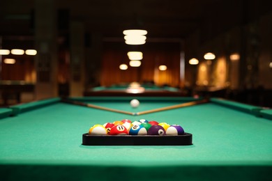 Photo of Plastic triangle rack with billiard balls and cues on green table indoors