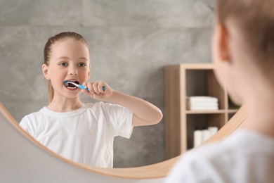 Photo of Cute little girl brushing her teeth with plastic toothbrush near mirror in bathroom