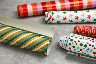Photo of Different colorful wrapping paper rolls on grey table, closeup
