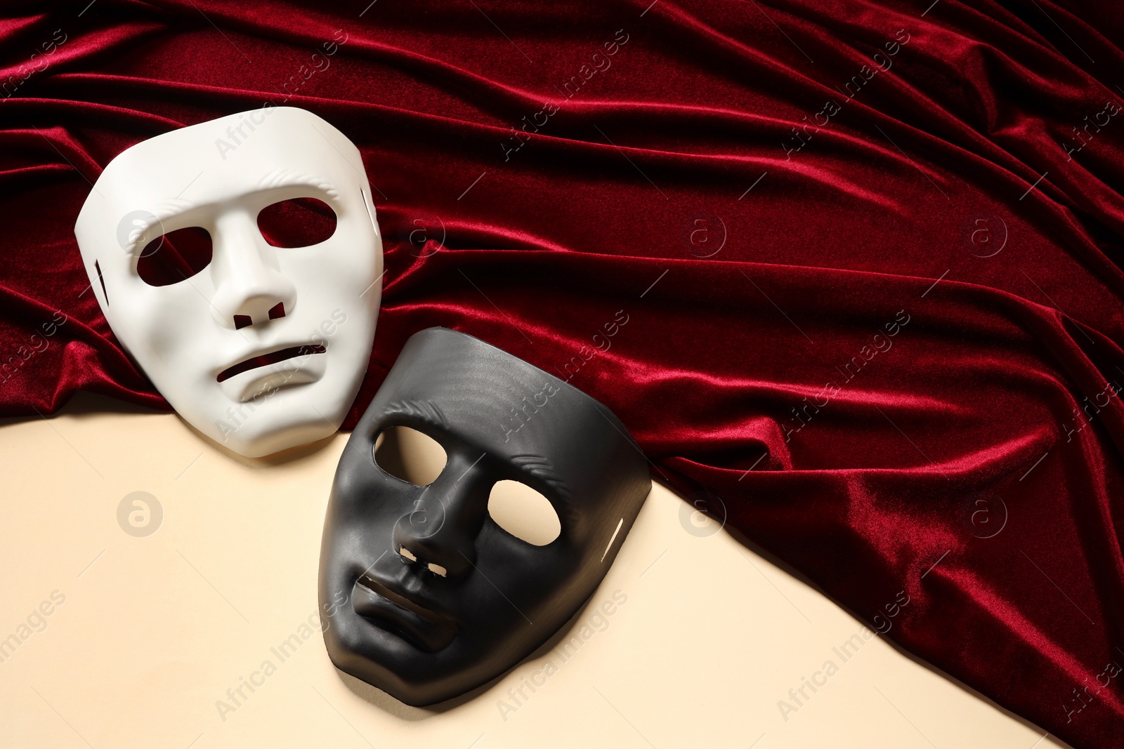 Photo of Theater arts. Two masks and red fabric on beige background, top view