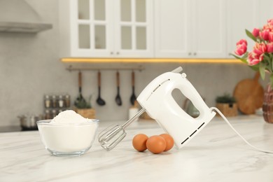 Photo of Modern mixer, eggs and bowl with flour on white marble table in kitchen