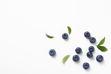 Photo of Tasty fresh blueberries with green leaves on white background, flat lay. Space for text