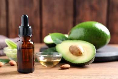 Bottle of essential oil, fresh avocado and almonds on wooden table, space for text