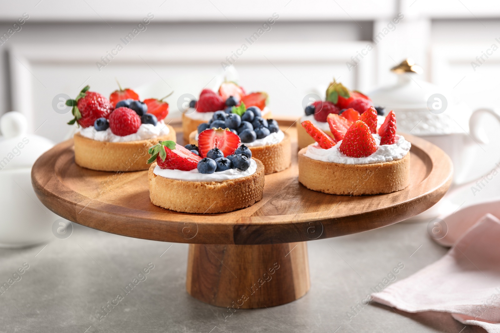 Photo of Cake stand with different berry tarts on table. Delicious pastries