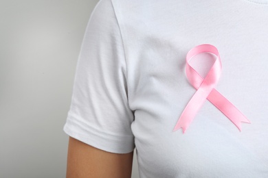 Woman with pink ribbon on grey background, space for text. Breast cancer awareness