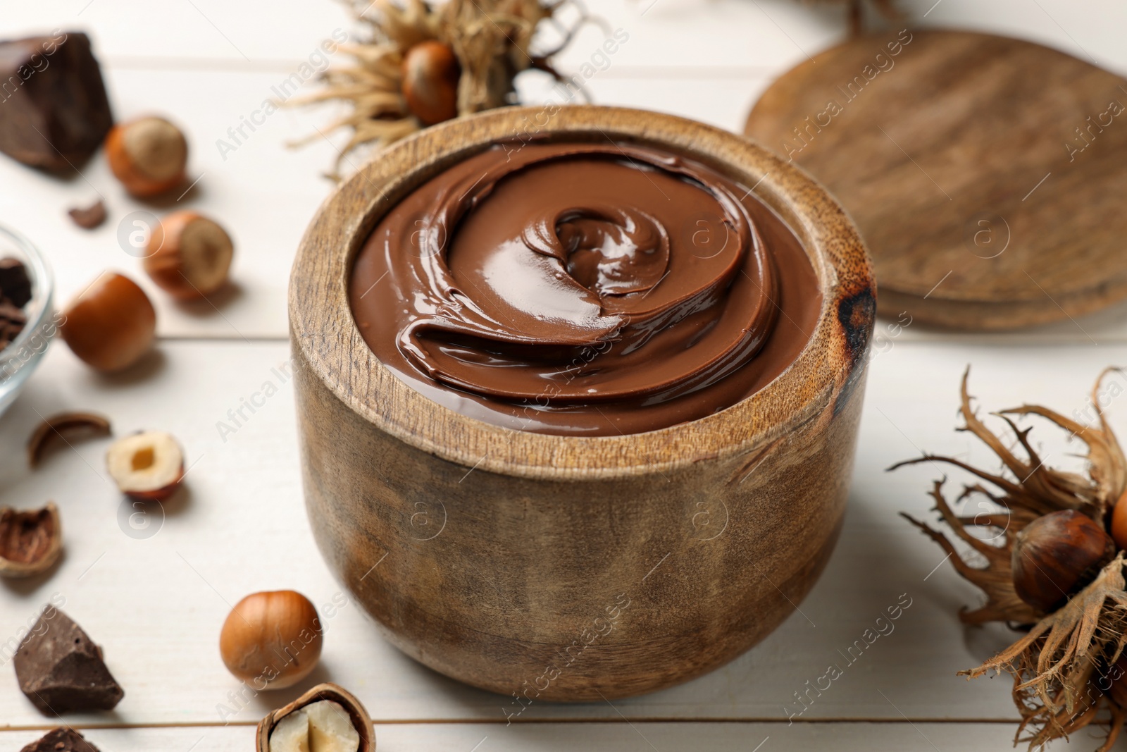 Photo of Bowl of tasty chocolate paste with hazelnuts on white wooden table