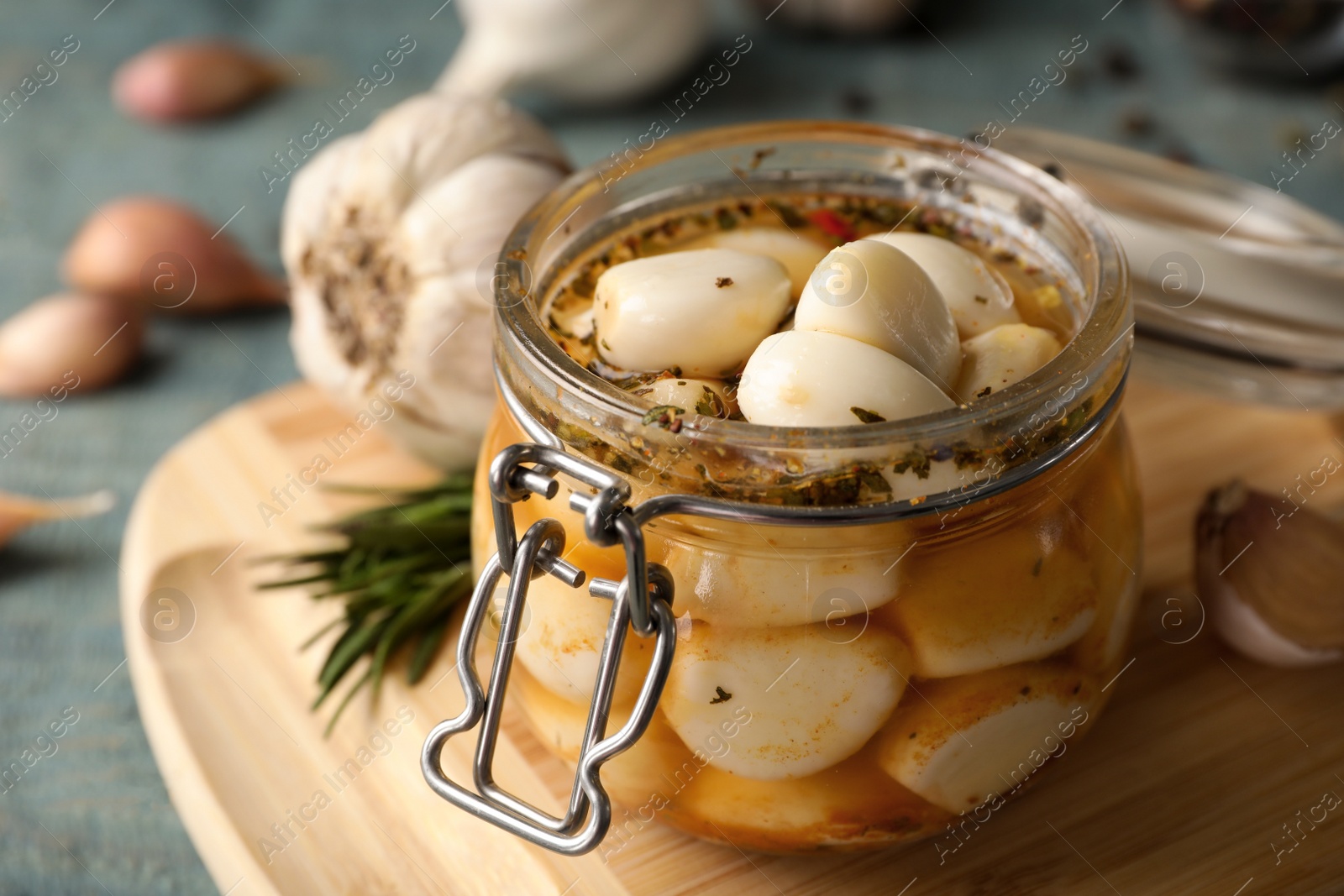 Photo of Preserved garlic in glass jar on wooden board, closeup