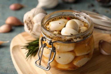 Photo of Preserved garlic in glass jar on wooden board, closeup