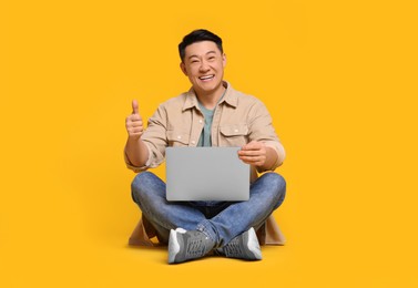 Photo of Happy man with laptop showing thumb up gesture on yellow background