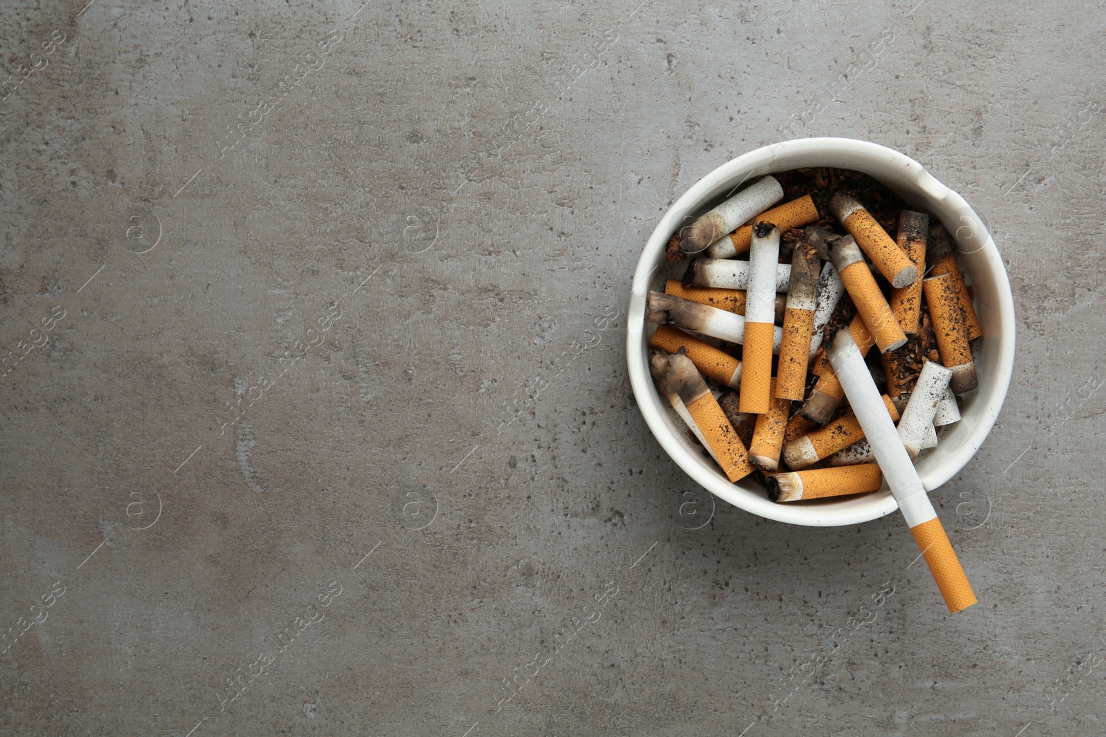 Photo of Ceramic ashtray with cigarette stubs on grey table, top view. Space for text