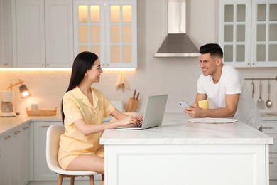 Photo of Happy couple wearing pyjamas with gadgets spending time together in kitchen