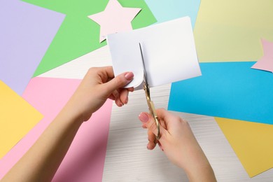 Woman cutting paper with scissors at white wooden table, top view