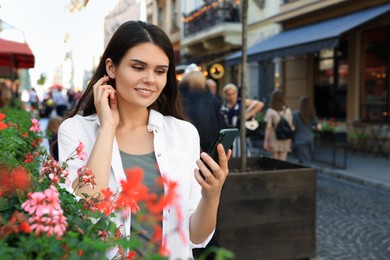 Photo of Young woman with smartphone near beautiful flowers on city street