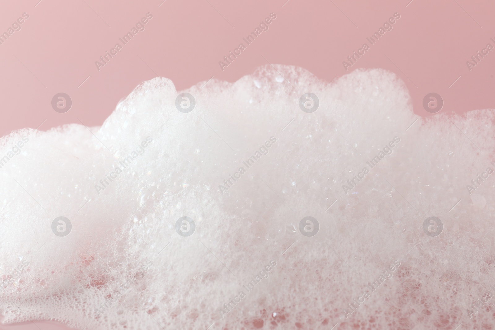 Photo of Fluffy bath foam on pink background, closeup